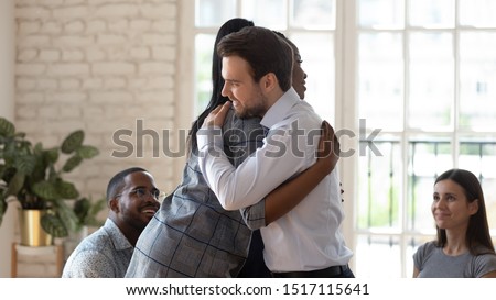 Smiling african american female employee hugging embracing happy coworker, giving support at group therapy session. Mixed race friendly teammates overcoming problems together, team building activity. Royalty-Free Stock Photo #1517115641