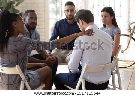Compassionate african american female employee putting hand on desperate coworkers shoulder, supporting, expressing condolence. Mixed race diverse team of workers sitting in circle on group therapy. Royalty-Free Stock Photo #1517115644