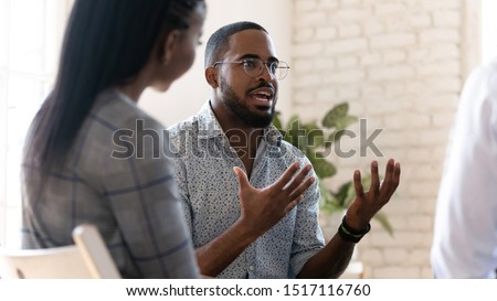 Head shot young african american male psychologist meeting patients at group therapy. Serious mixed race counselor giving advices to employees. Confident business coach training staff at office. Royalty-Free Stock Photo #1517116760
