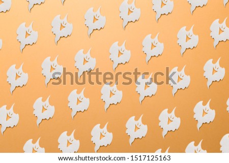 Halloween decorations. Trendy pattern made with paper ghosts on bright light orange background. Minimal style with colorful paper backdrop. Minimal creative concept