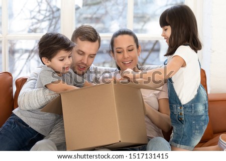 Curious happy parents holding big carton box, unpacking delivery parcel with joyful little daughter and son. Cheerful family buyers received order from popular online internet store, looking inside. Royalty-Free Stock Photo #1517131415