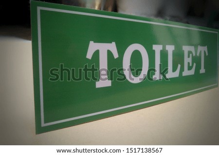 green acrylic information board that reads "TOILET" with a blur background