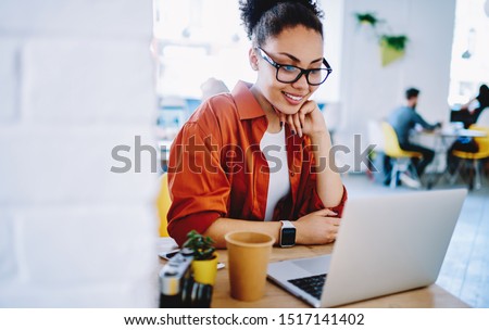 Positive dark skinned hipster girl enjoying friendly video call on laptop computer using web camera for communicating, happy woman watching comedy video on netbook during free time on leisure Royalty-Free Stock Photo #1517141402