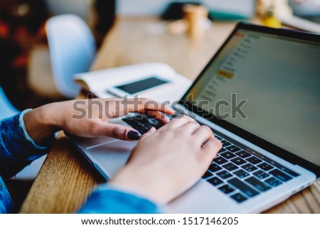 Cropped image of female hands typing email on keyboard of laptop computer while connected to wireless internet, woman searching items on web store during shopping online via new modern netbook