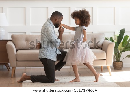 In cozy living room african dad got down on one knee kisses hand of daughter princess wearing fluffy pink skirt, chivalrous gesture, courtesy and politeness, devotion admiration, good manners concept Royalty-Free Stock Photo #1517174684