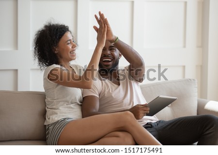 Excited african wife gives high five husband holding tablet computer, young couple celebrating fantastic received opportunity, bank approve loan e-mail, booked hotel for future vacation travel concept Royalty-Free Stock Photo #1517175491