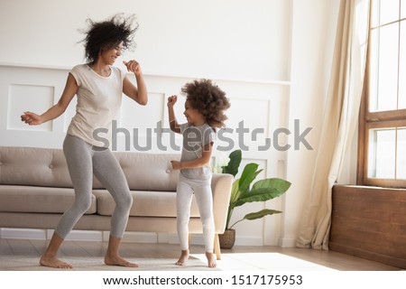 African daughter and mother dancing in modern cozy sunny living room, babysitter and little kid enjoy summer day at home, family celebrating vacation, leisure, funny mood, happy active people concept Royalty-Free Stock Photo #1517175953