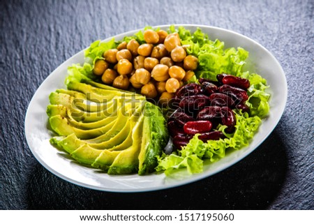 Vegetable salad with chickpea, avocado and red beans in bowl on black stone