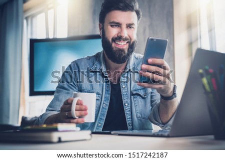 Manager having break in office and communicating with online friend in social network on smartphone. Guy taking selfie at workplace on mobile phone. Smiling man watching funny video on wireless device