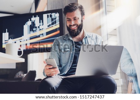 Male professional working on laptop and smartphone in office. Digital developer testing apps and synchronizing corporate programs. Manager taking selfie at workplace and posting images in social media