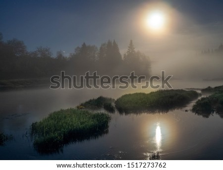 The light of full moon scatters on the lake through the fog