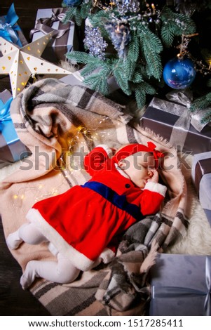 An infant dressed like a little Santa sleeping under the Christmas tree