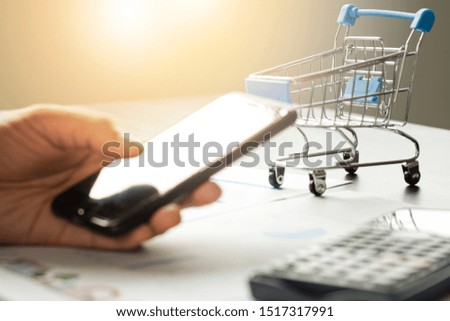 E-commerce and Online shopping concept. Hand holding mobile phone typing online order to shopping with trolley cart.