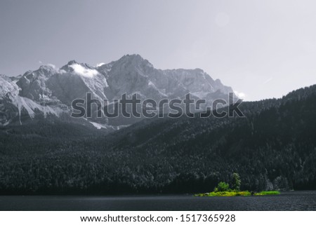 Black and white photo Zugspitze with small island on lake being the only color, green. 