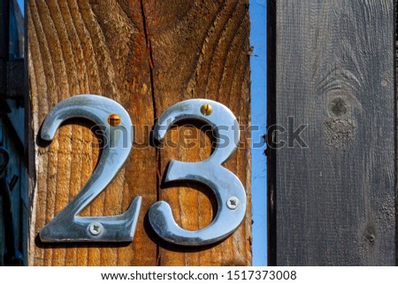 Shiny silver house number 23 on a gate outside a house