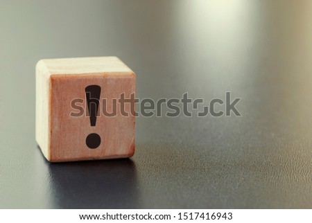 Small wooden block with exclamation mark in black on the side over a grey background with highlight and copy space Royalty-Free Stock Photo #1517416943