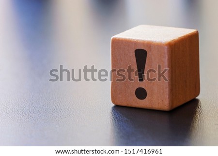 Warning exclamation mark on a wooden block to attract attention over a grey background with beams of light and copy space Royalty-Free Stock Photo #1517416961