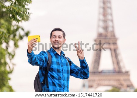 A happy European man in a shirt takes a funny selfie against the Eiffel tower in France. Travel and leisure concept