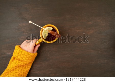 Flat lay autumn composition with woman hand in a warm woolen sweater holding a cup of tea over woodent background. Comfort for the cold weather