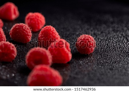 Chaotically scattered ripe raspberries on a black surface with water droplets. Close up.