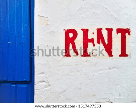White wall with word rent written with red letters and wooden blue door.