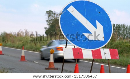 roadworks cone flashing on UK motorway at evening with traffic passing
