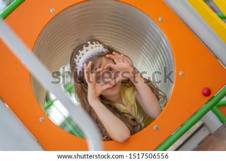 Young beautiful princess girl lies in the orange tunnel and shows heart sign with her fingers throught her face.