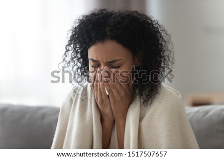 Close up african woman sit on couch covered with warm plaid holding handkerchief blowing runny nose to relief stuffy nose feels unhealthy having vitamin deficiency avitaminosis, seasonal flu concept Royalty-Free Stock Photo #1517507657