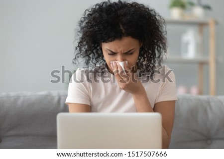 African woman solve business matters on sick leave, self-employed female sit on couch work on laptop, less productive caused by sickness, blow runny nose feels unhealthy, allergy seasonal flu concept Royalty-Free Stock Photo #1517507666