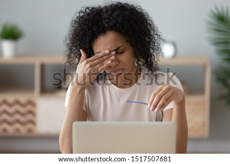 Close up view african unhappy woman sitting near computer take break during workday took off glasses frown face feel unhealthy, closed eyes to relief painful sensations dry tensed eye strain concept Royalty-Free Stock Photo #1517507681