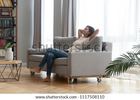 In modern living room peaceful african woman resting leaned on sofa closed eyes put hands behind head feels placidity enjoy weekend or vacation, inner harmony, no stress anxiety fatigue relief concept Royalty-Free Stock Photo #1517508110
