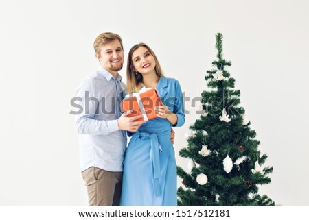 Holidays and celebrations concept - Cute young couple exchanging Christmas presents in front of a christmas tree
