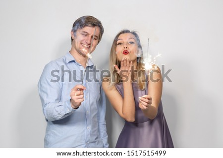 Party, new year, christmas and holidays concept - young couple holding sparklers on white background