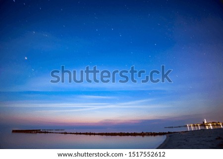 The last vibrant colors of the sunset still visible while the first stars appear at Hindeloopen, IJsselmeer in the Netherlands. The sky is scattered with clouds reflecting in the water.