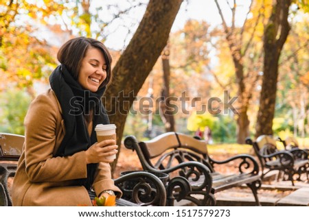 woman sitting on the bench at autumn city park drinking coffee fall season