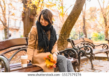 woman sitting on the bench at autumn city park drinking coffee fall season