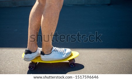 Legs in white sneakers are on a yellow skateboard with purple wheels. The correct setting of the legs on a skateboard. Half frame in the shadow, side view.