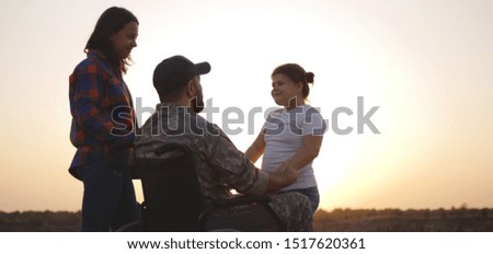 Full shot of a wheelchaired soldier kissing his wife and hugging his daughter on a meadow