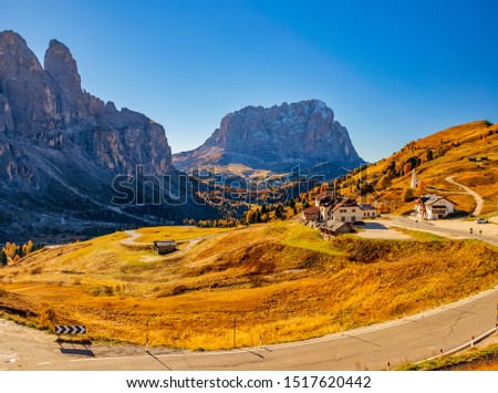 Amazing panoramic view on Sassolungo (Langkofel) mountain and Gardena Pass at sunny autumn day. Winding road among yellowed pasture. Dolomite Alps, South Tyrol, Italy