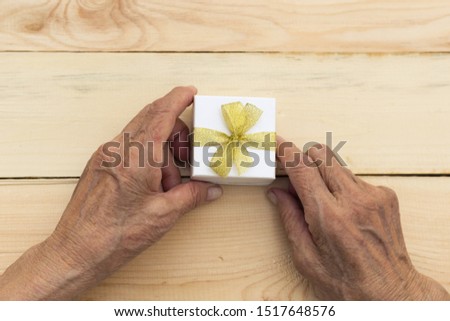 Hands of an elderly man holding a gift box. The concept of attention and care for old people, festive joy, giving a gift for a birthday or new year. Image. Royalty-Free Stock Photo #1517648576