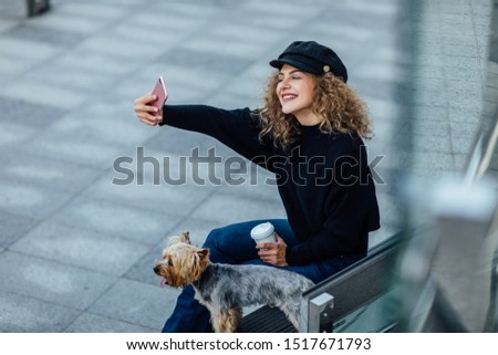 Young beautiful woman with Yorkshire Terrier make a selfie, against green of summer city have a break time. Woman with her phone.