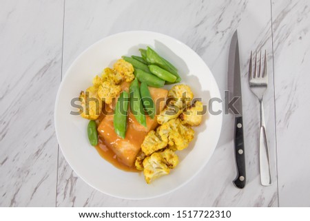 top down view of a plate of baked fish halibut with cauliflower and pees with cutlery