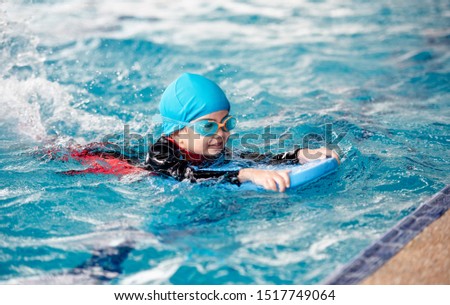 One girl wearing a swimsuit uses a foam pad to practice swimming in a swimming pool with a teacher. She happily and smiling. Royalty-Free Stock Photo #1517749064