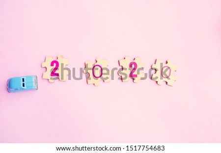 Blue toy car and jigsaw puzzles with 2020 numbers signify stepping into the new year on pastel pink backgrounds.