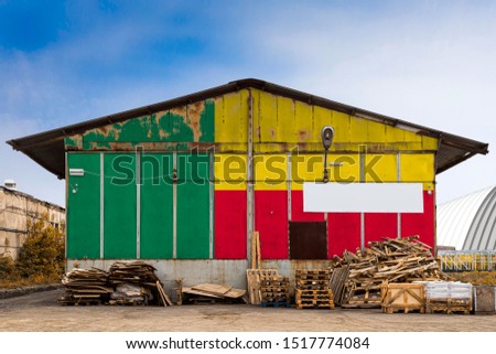 Close-up of the national flag of Benin
 painted on the metal wall of a large warehouse the closed territory on a summer day. The concept of storage of goods, entry to a closed area, tourism