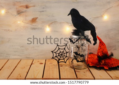 holidays image of Halloween. bats, black crow and witch hat over wooden table