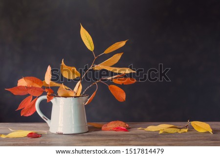 autumn leaves in jug on wooden table on dark background