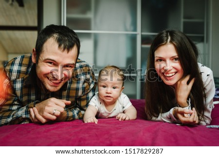 Happy family, parenthood and people concept - mother, father with baby lying in bed at home. Portrait of young smiling family with son.