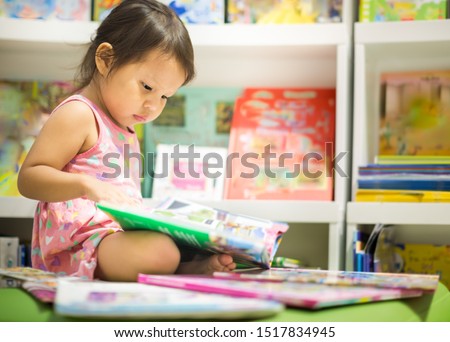 Little girl reading next to a stack of books in the  library.