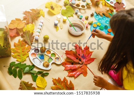 Girl paints leaves. Gouache, brush and various autumn leaves, Children's art project. Colorful Hand-painted on dry autumn leaves